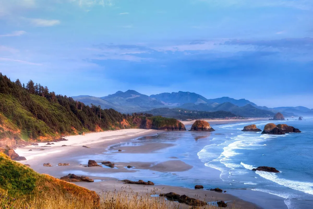 This view image highlights the breathtaking scenery of distant mountains, rugged rock formations, ocean waves, and a sandy beach—perfect for beachcombing, hiking, or simply soaking up the tranquility of the Oregon coast.