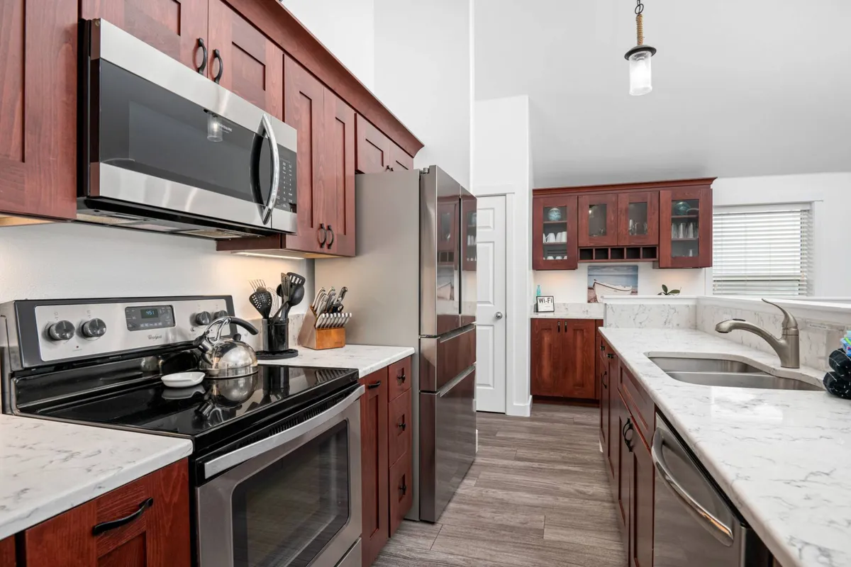 A contemporary kitchen scene featuring stainless steel appliances, marble countertops, and rich dark wood cabinetry. The kitchen is open to the living and dining spaces, inviting family cooking, entertaining, and social connection. The setting feels modern, functional, and inviting.