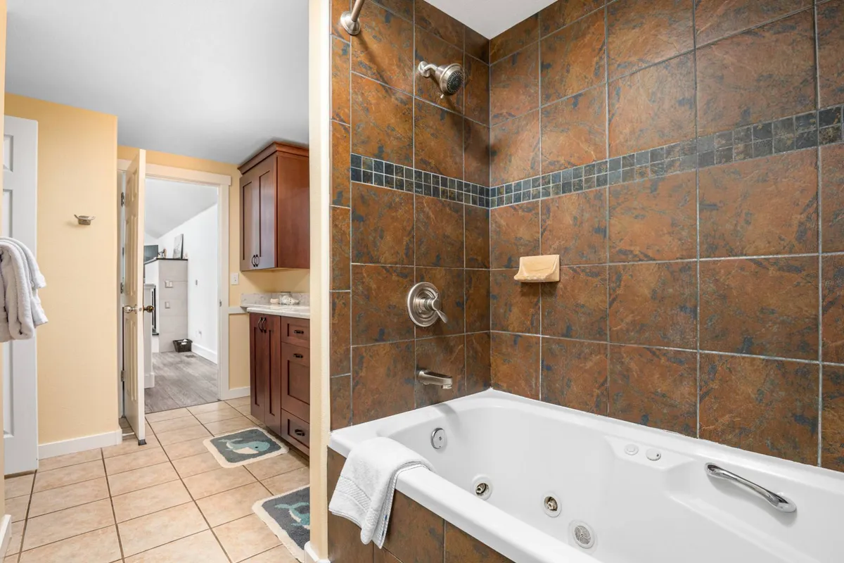 A tranquil bathroom featuring a jacuzzi tub with textured wall tiles and wood cabinetry, creating a spa-like atmosphere. The space invites relaxation and self-care, suggesting leisurely soaks and peaceful mornings.