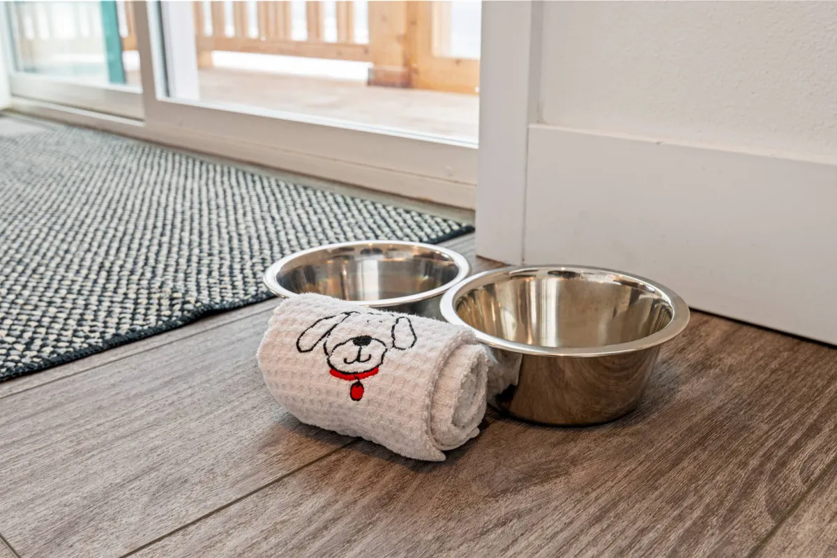 A cozy interior corner featuring two dog bowls and a dog towel set out on the floor, signaling a welcoming environment for pets. The soft lighting and accessible layout make it clear that furry guests are catered for and comfortable.