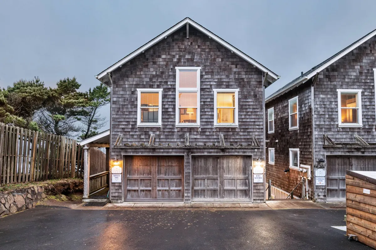 A warmly lit shingle-style exterior with large windows, garage doors, and a porch perfect for gatherings. The setting is ideal for sharing meals, watching sunsets, or heading out to explore nearby trails.